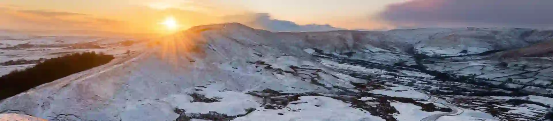 View of the Peak District at winter, with snowy mountains and the sun creeping over the edge of the land