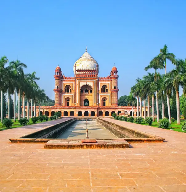 Front view of Humayun's Tomb in Delhi, India, framed by symmetrical rows of palm trees and a long reflecting pool under a clear blue sky