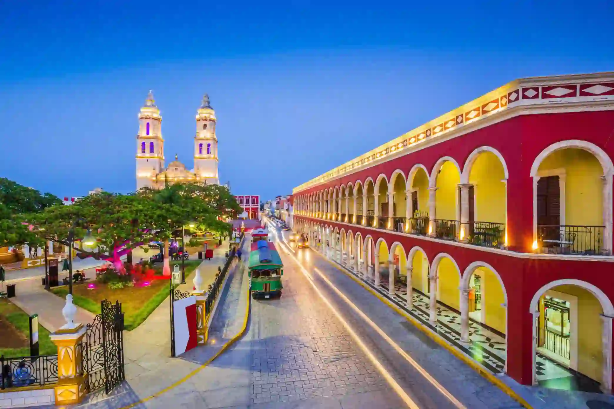 Brightly lit colonial buildings and a cathedral illuminate the street of the historic town of Campeche in Mexico during twilight
