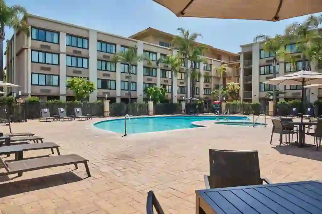Courtyard view of DoubleTree by Hilton Buena Park featuring an outdoor pool framed by sun loungers and umbrellas, with guest rooms overlooking the pool area