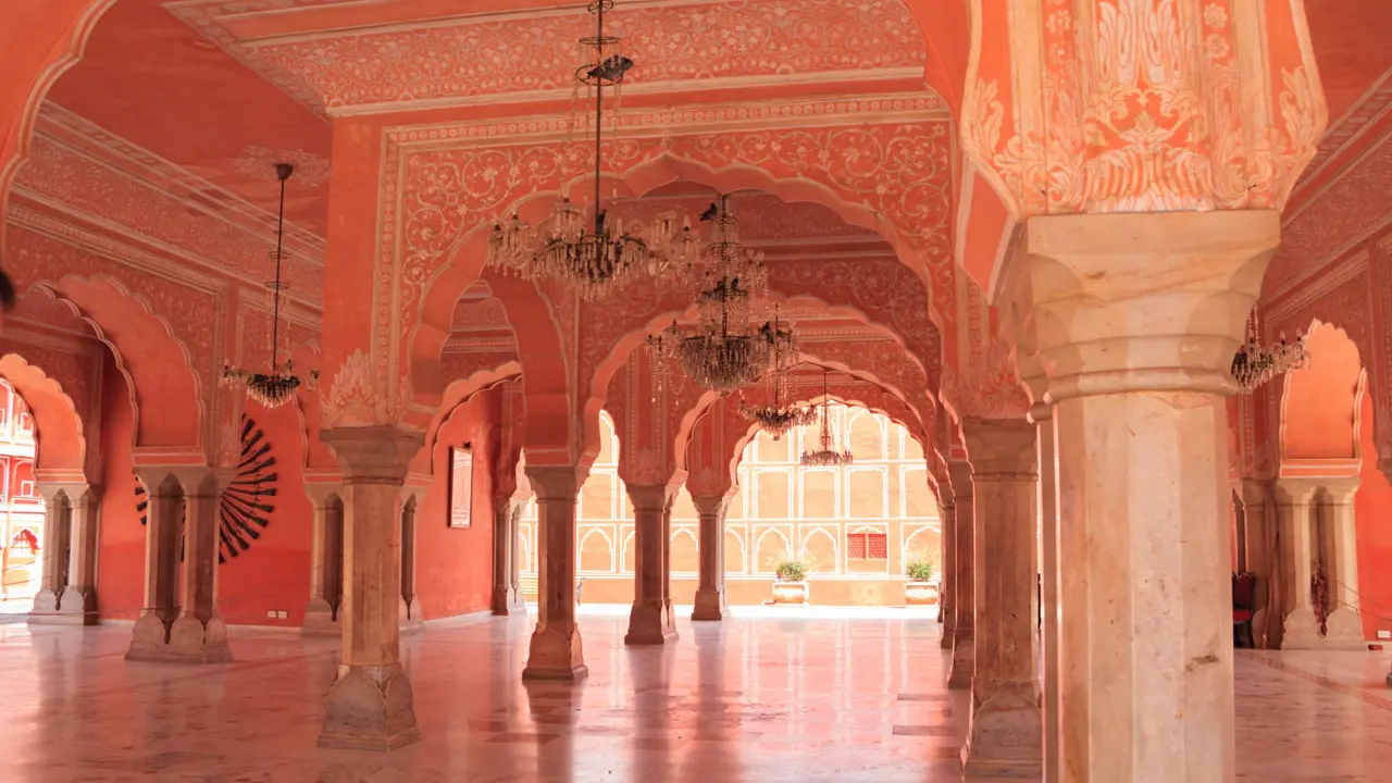The elegant interior of the City Palace in Jaipur, featuring intricately decorated pink arches, marble floors, and hanging chandeliers under the palace’s domed ceilings