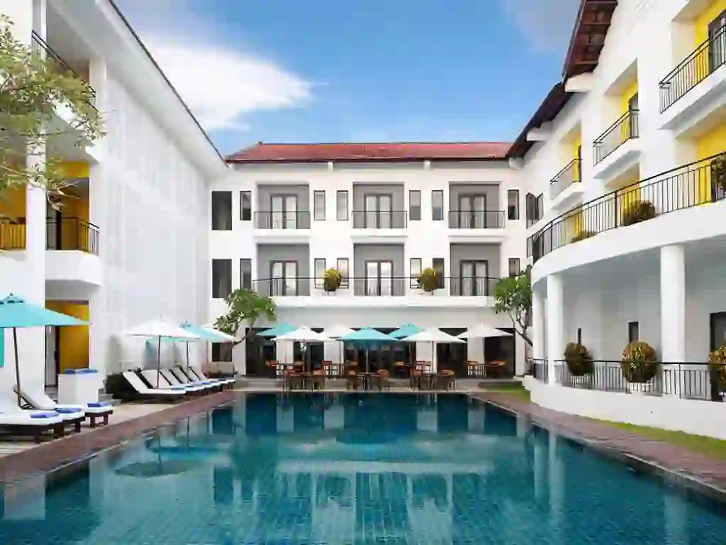 Exterior of Hotel ÊMM Hoi An featuring private balconies overlooking a swimming pool surrounded by sun loungers