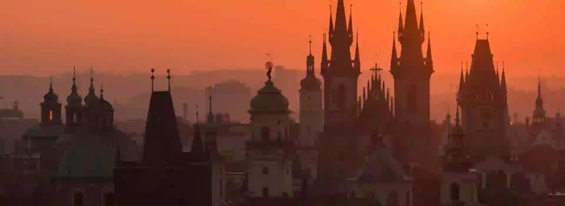 Prague cityscape against an orange sky with silhouettes of tall buildings with spiked turrets