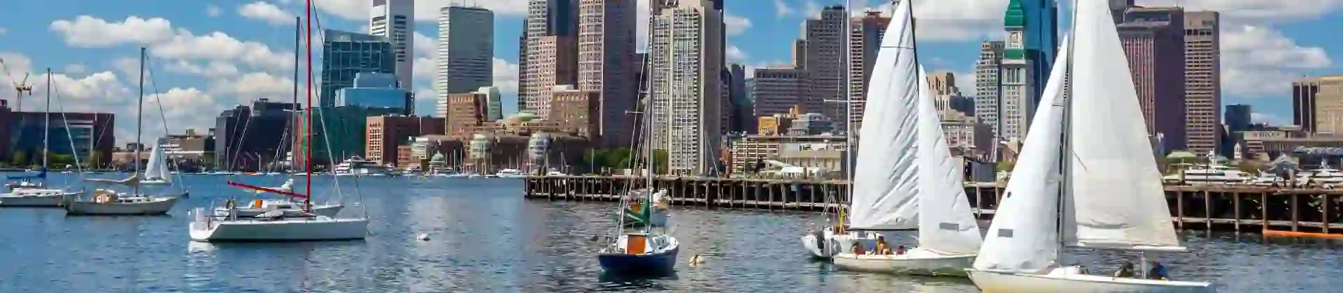 View of Boston, Massachusetts, seen across the water from Pier Park, with the city skyline rising above the harbour under a partly cloudy sky