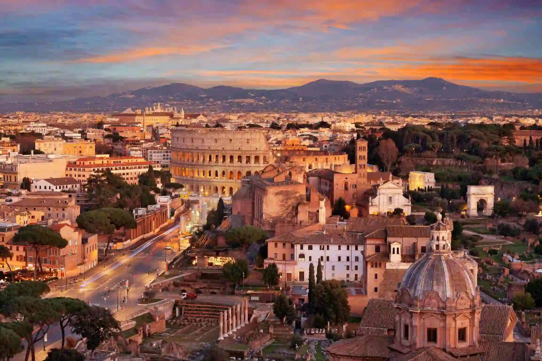Cityscape of Rome at sunset, showing the Colosseum and St. Peter's Basilica
