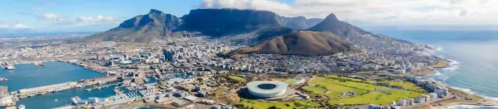 Aerial view of Cape Town, South Africa, showing the city nestled between Table Mountain and the Atlantic Ocean, with the coastline, harbour, and urban landscape clearly visible