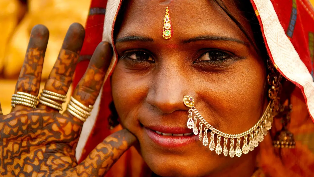 A Rajasthani woman smiles, wearing bright traditional jewellery and a colourful headscarf in Rajasthan in India