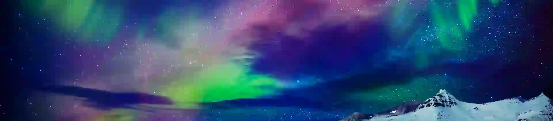 Starry sky with green, purple and blue Northern Lights. Below, a lake and a snowy mountain