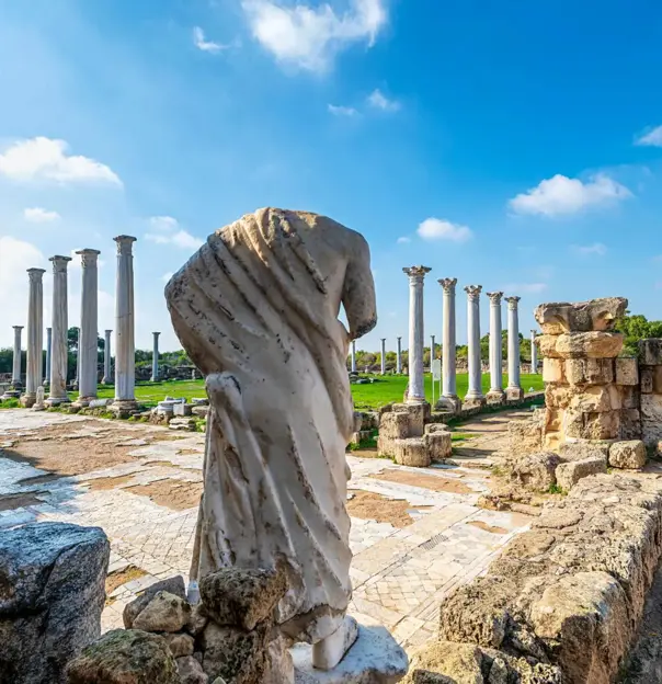 View of Roman ruins in Salamis, with the back of a headless marble statue. Further away, there is a green lawn surrounded by marble pillars