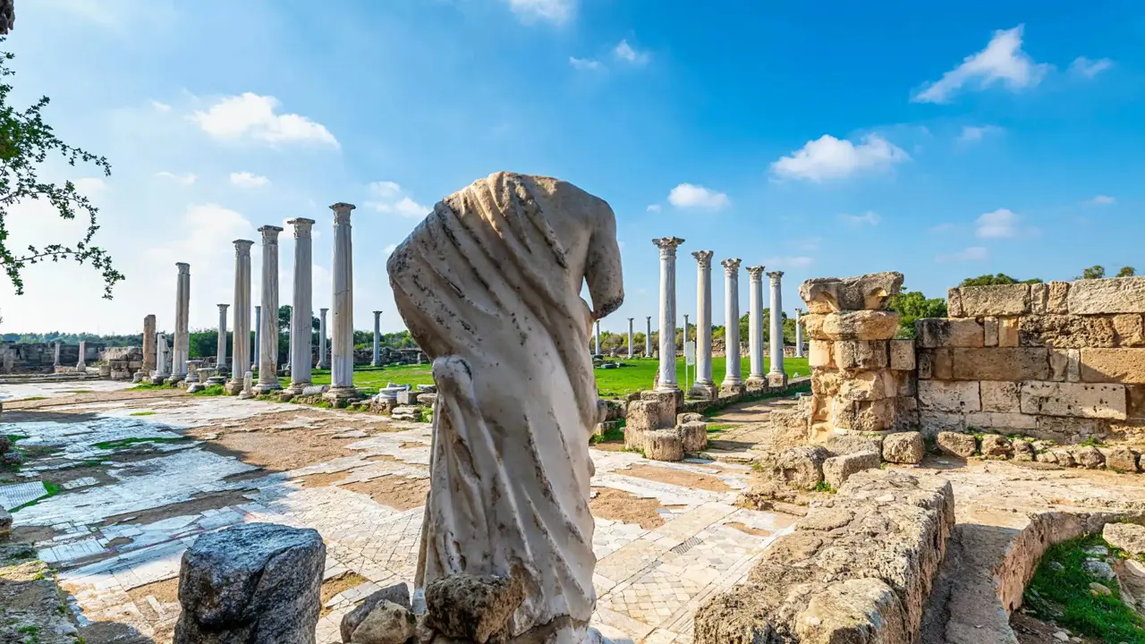 View of Roman ruins in Salamis, with the back of a headless marble statue. Further away, there is a green lawn surrounded by marble pillars