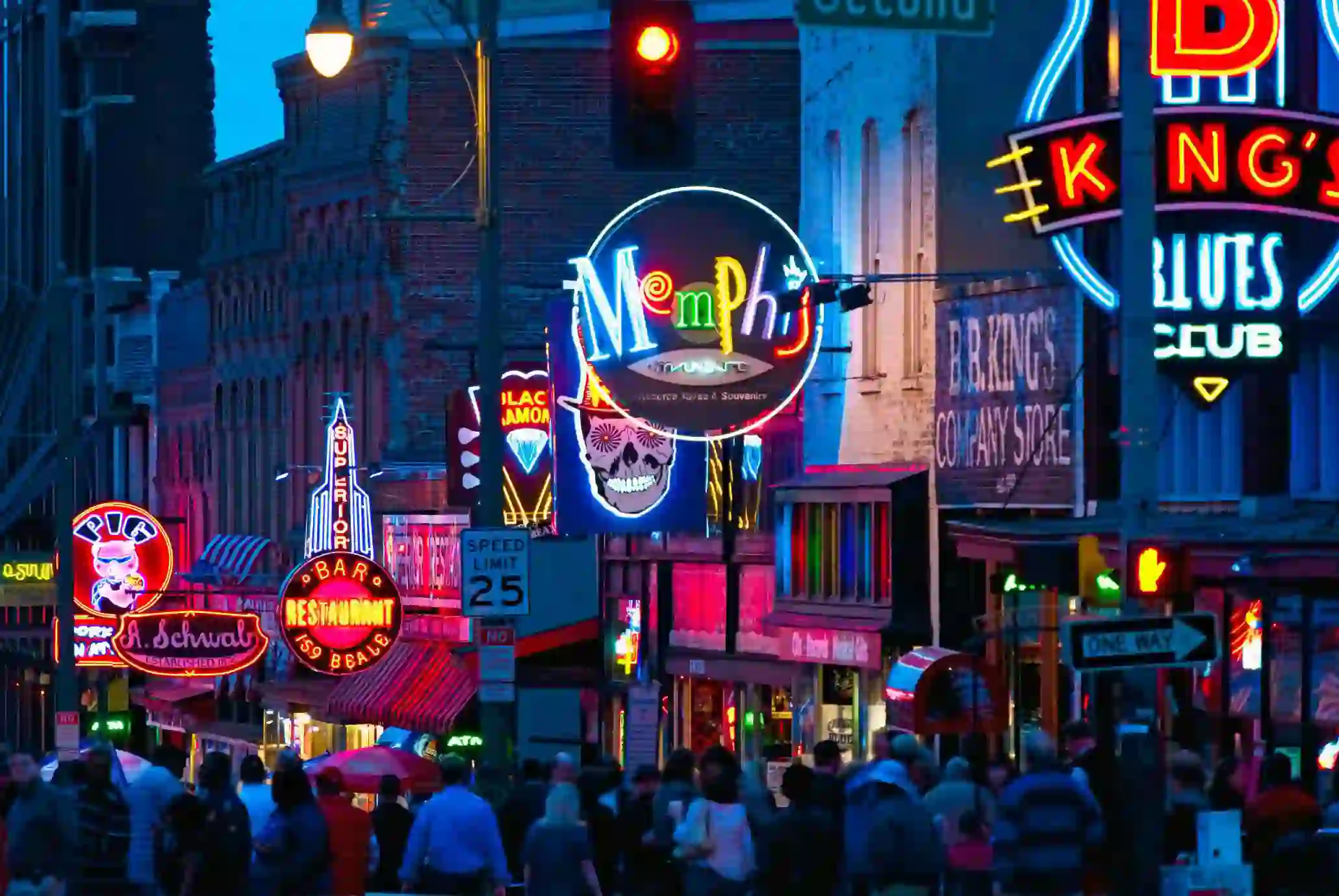 Vibrant night scene of Beale Street in Memphis, Tennessee, with colourful neon signs for bars, restaurants, and blues clubs, and a crowd of people walking along the street