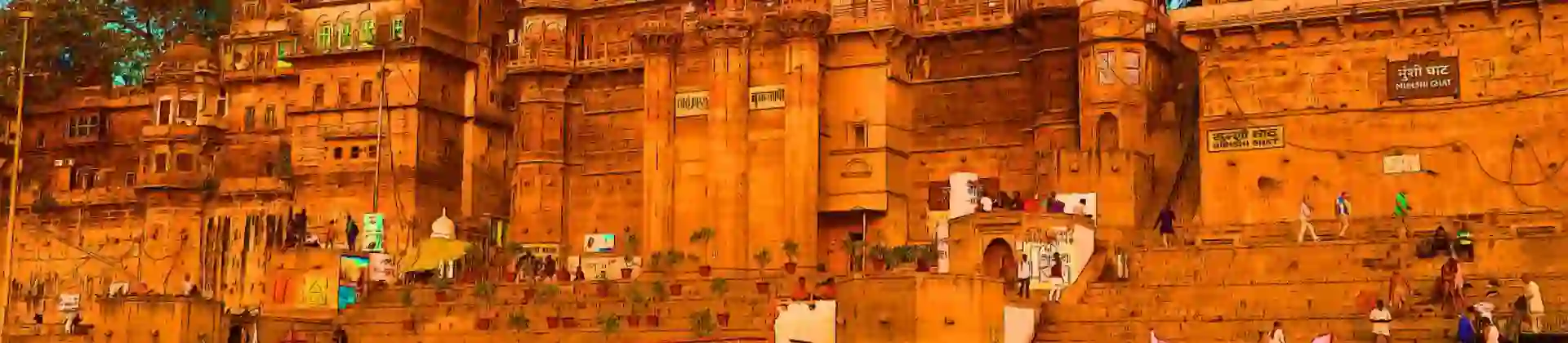 The ghats of Varanasi seen from the River Ganges, with historic sandstone palaces and colourful boats reflecting in the calm evening water