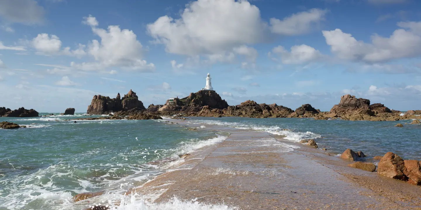 Long shot of the La Corbiere Causeway Light house, showing the sea below it, the rocks either side of it and a stone panel which runs towards it across the water