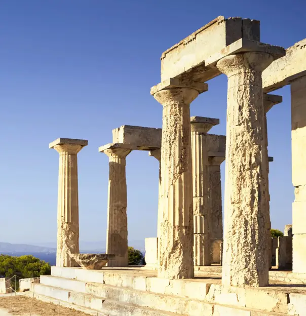 Ancient Greek temple ruins on an island with weathered stone columns overlooking the blue sea and distant mountains under a clear sky